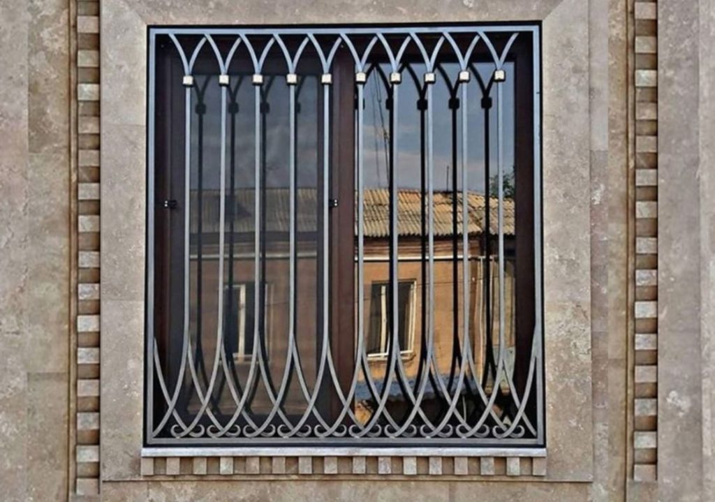 Art deco style window grill. Stone wall and window showing the building in the background. 
