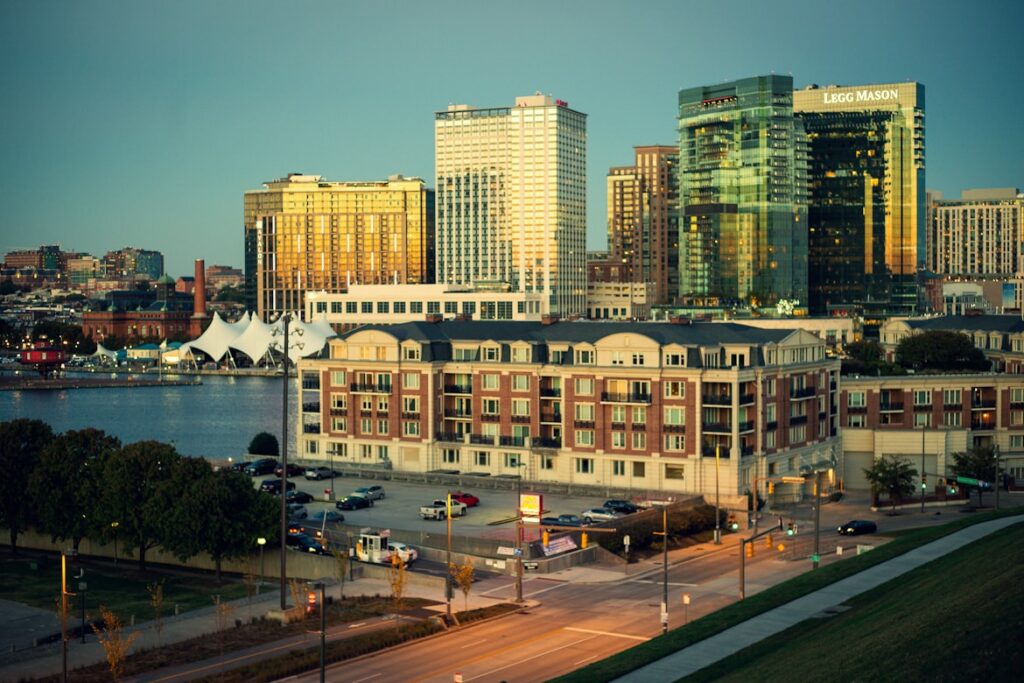 Baltimore's Inner Harbor at golden hour, with the Legg Mason tower and waterfront buildings catching warm light behind a historic brick apartment complex.