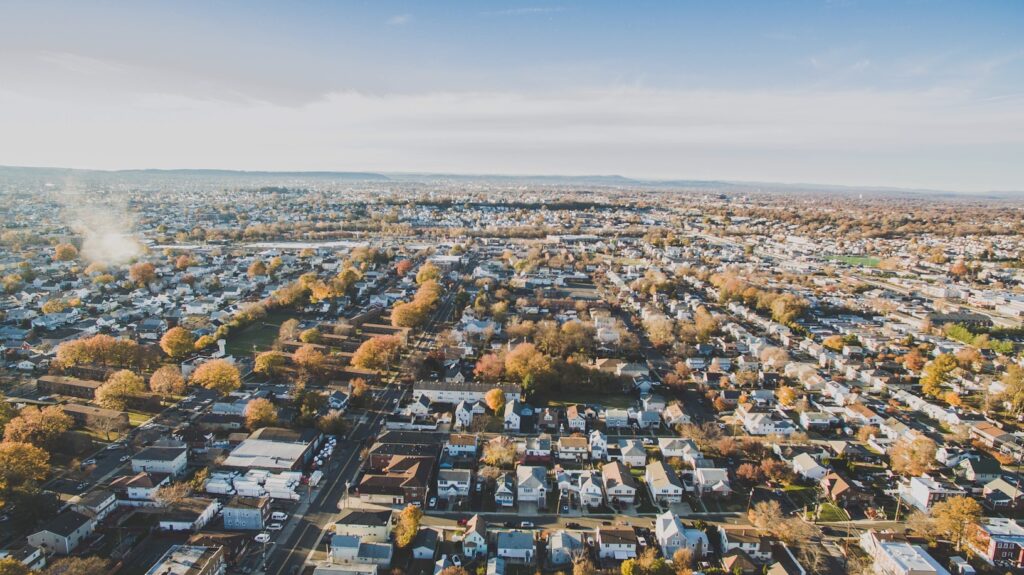 An aerial view of a New Jersey suburb in autumn, with rows of houses, scattered trees in fall color, and a hazy skyline in the distance.