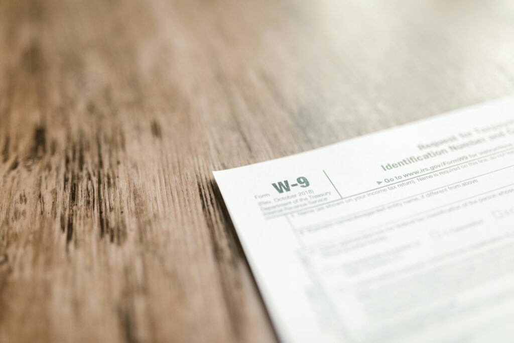 A W-9 tax form rests on a wooden surface, with shallow focus blurring most of the text.