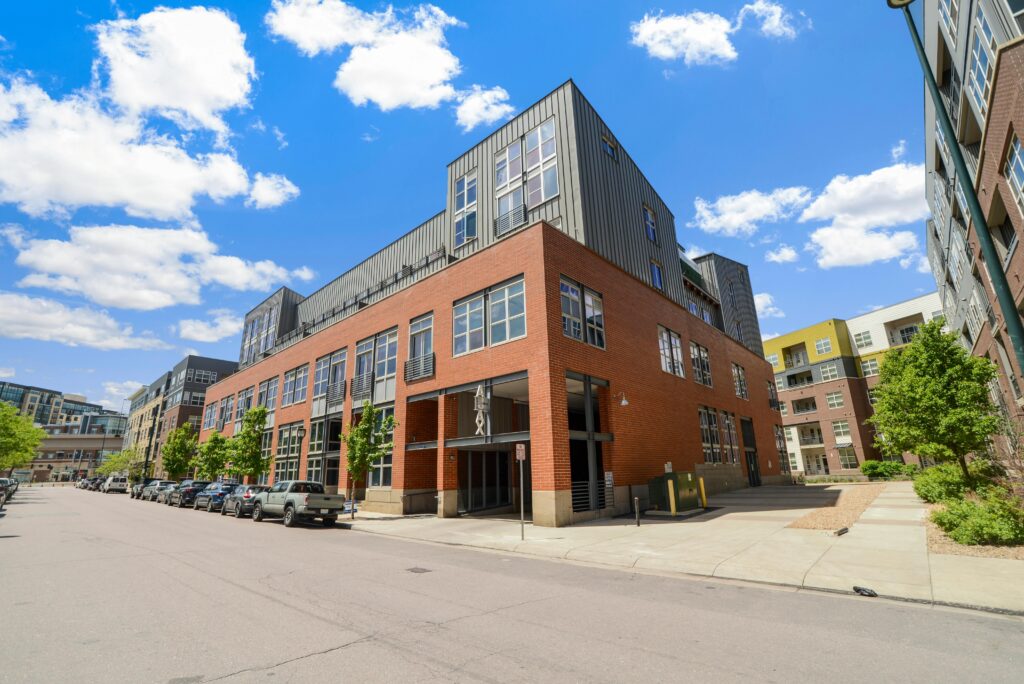 A red brick industrial building converted into lofts, with large factory-style windows and a modern gray addition built on top, located on a city street.