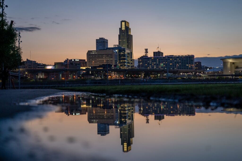 The Omaha skyline at dusk, with the First National Bank Tower and surrounding buildings reflected in still water below.