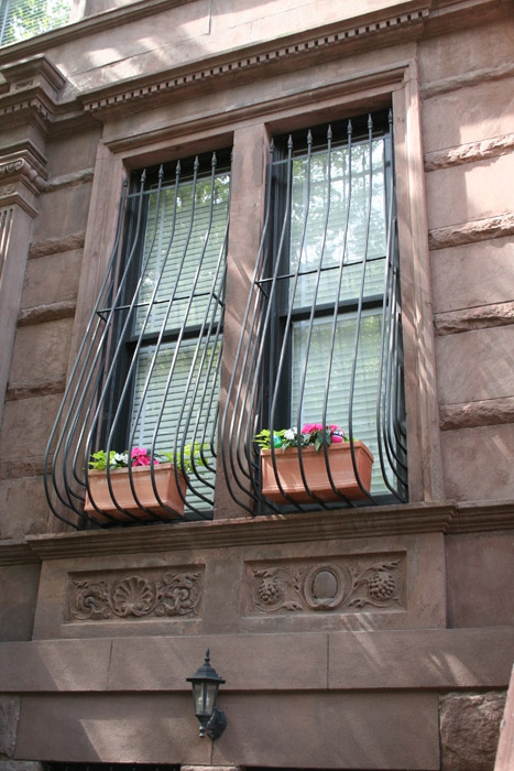 Curved window grill with plants. A window and a brown wall in the background. 