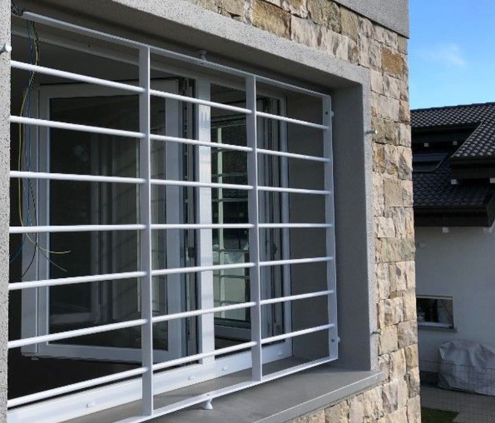 A window with white bars over it. A stone wall and white walls in the background. 