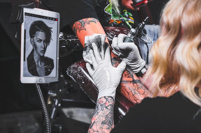tattoo artist tattooing a face onto the arm of a client