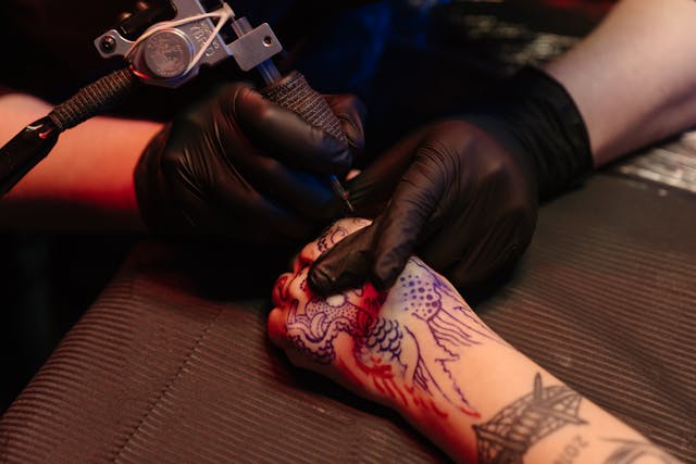 tattoo artist tattoing a client's hand