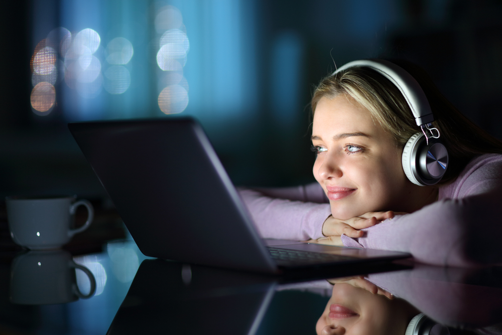 Satisfied teen wearing headphones watching media on laptop in the night at home