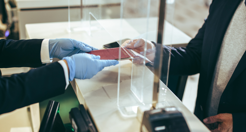 Closeup of airline check-in counter at airport. Traveler giving his passport to airport staff for checking in for the flight during pandemic.