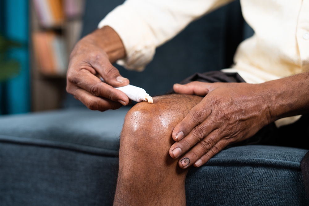 Close up of unknown old man applying cream for knee pain at home - concept of treatment or treatment for osteoarthritis and knee sprain