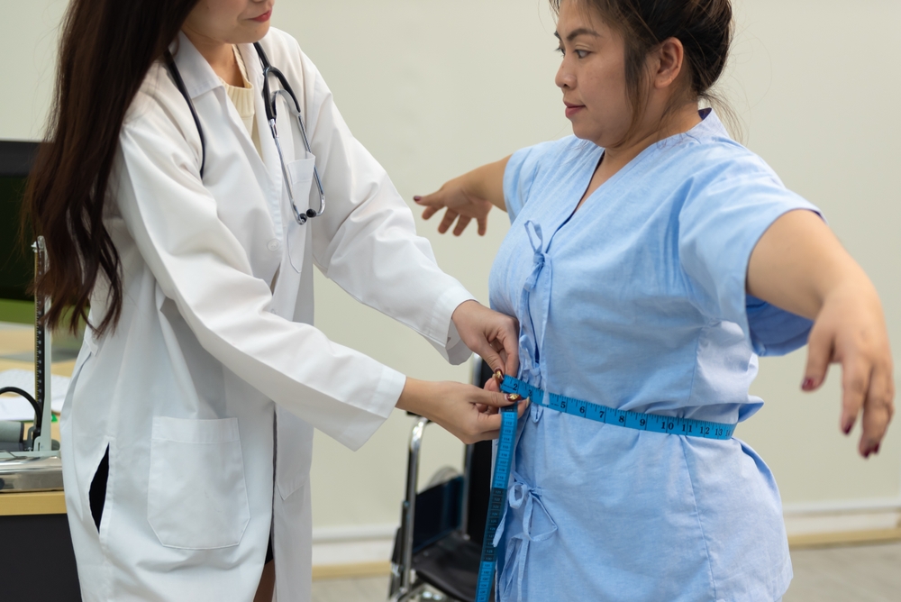 An Asian female doctor examining an obese woman's body in a hospital.