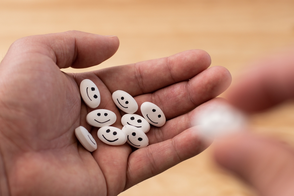 Hand drinking white medicine pill with focus on happy face on pills with bokeh background