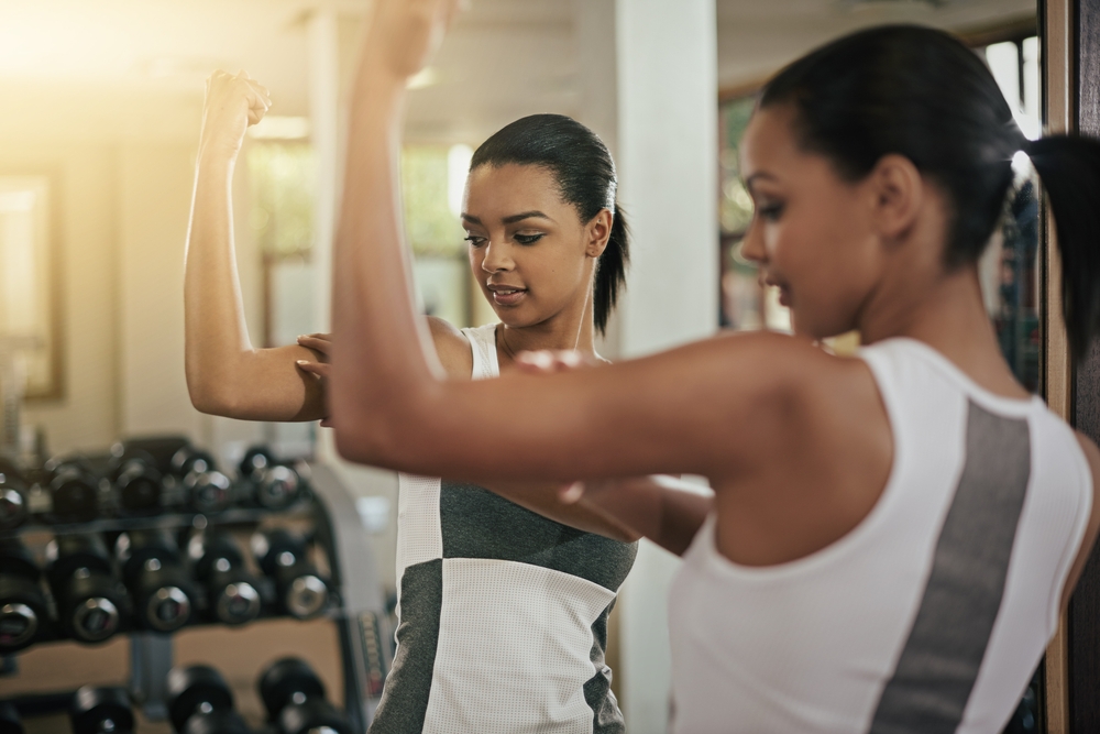 Woman, reflection or flexing in mirror at gym with fitness, workout and exercise of bodybuilder with growth. Progress, strong or confident girl athlete with sport training, wellness or bicep muscle