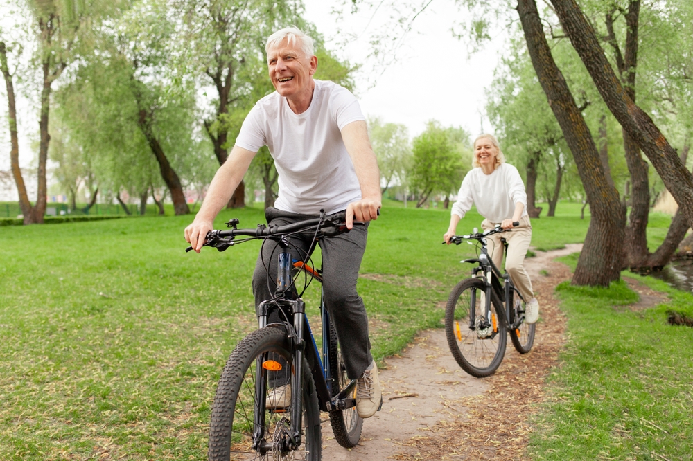 elderly senior couple rides bicycle in the park in the summer and smiles, old gray-haired man and woman are actively resting outdoors, old people practice cycling in forest