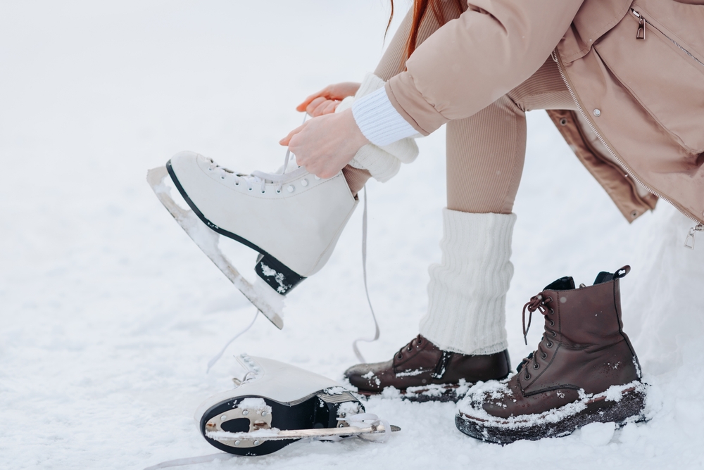 young girl in white and beige winter clothes lacing up skates before skating in ice rink in winter cloudy snowy day