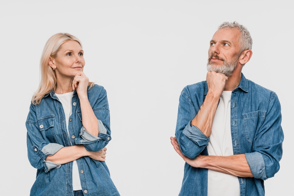 Puzzled pensive couple two friends elderly gray-haired man blonde woman in denim casual clothes standing looking up put hand prop up on chin isolated on white color background studio portrait