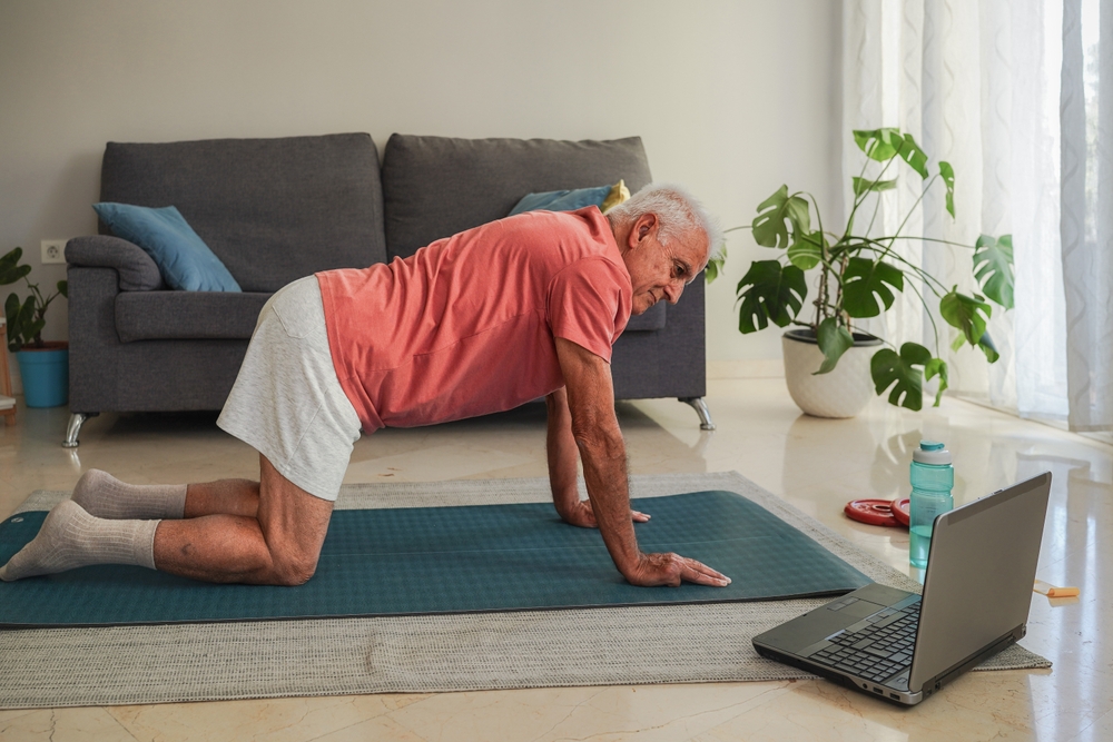 Active senior man exercising at home with online coach using laptop