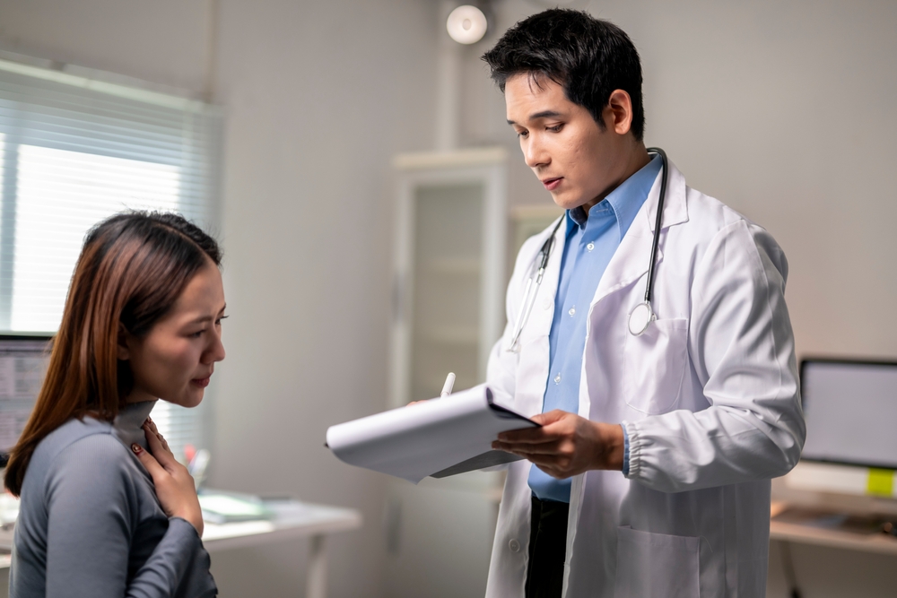 A doctor is talking to a woman in a hospital room. The doctor is holding a clipboard and the woman is holding her arm out. Scene is serious and concerned