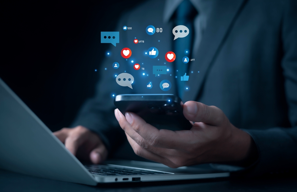 Businessman using smartphone with social media icons, likes, comments, and shares, representing digital marketing, online communication, engagement, social networking, and mobile technology.