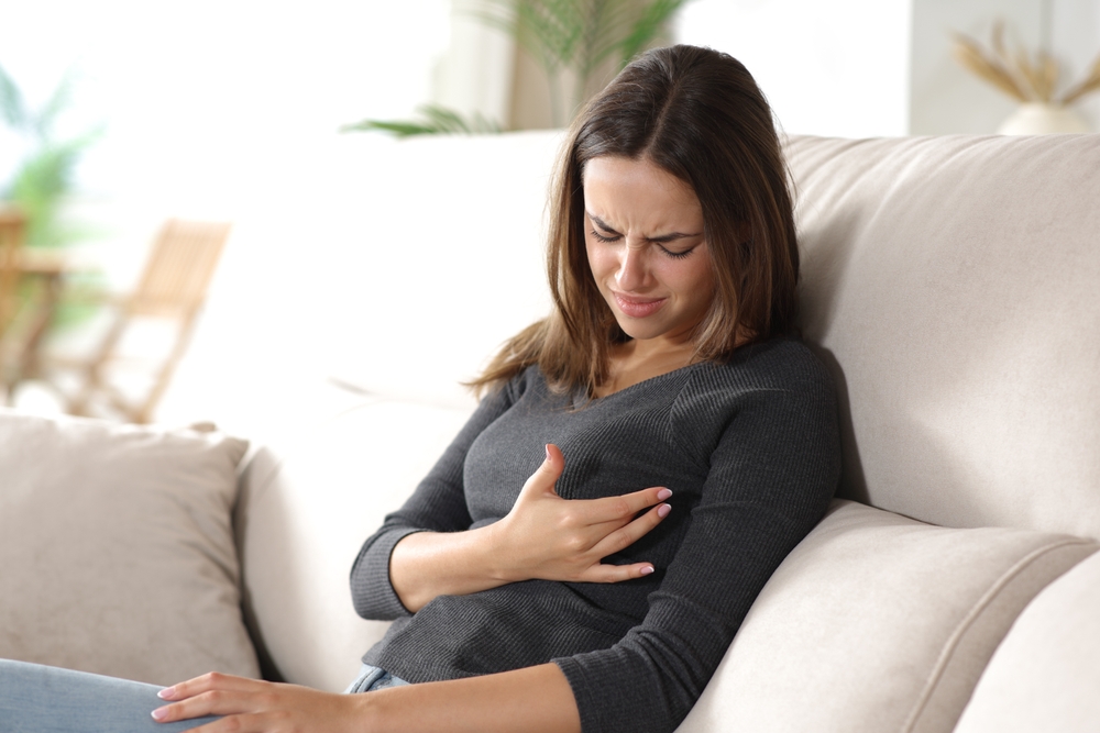 Depressed woman with breast pain sitting on sofa at home
