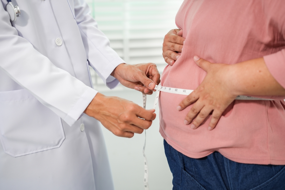 A doctor measures an Asian woman's waist during a routine health check-up to assess abdominal fat, obesity risk, and overall health status as part of preventive healthcare and weight management.