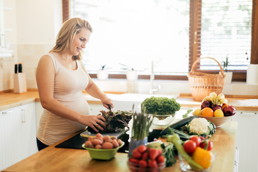Beautiful pregnant woman preparing food in island kitchen with fresh ingredients