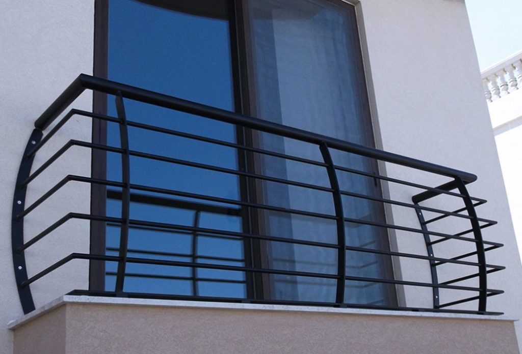 Balcony with bars and glass door. Curtains and white walls in the background. 