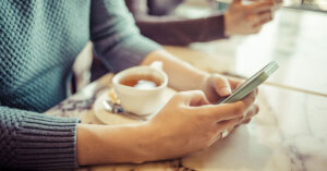 Someone May Be Spying on You If These Apps Are Still on Your Phone person using smartphone in coffee shop