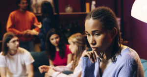 Young black woman sitting alone feeling sad and left out at a party with friends