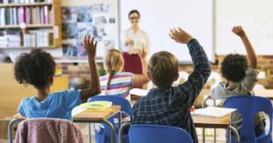 children in classroom raising their hands