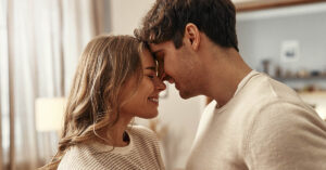 Why Being in a Nurturing Relationship Could Help You Heal Faster Young couple in love standing face to face tenderly hugging in the living room at home. Romantic evening together.