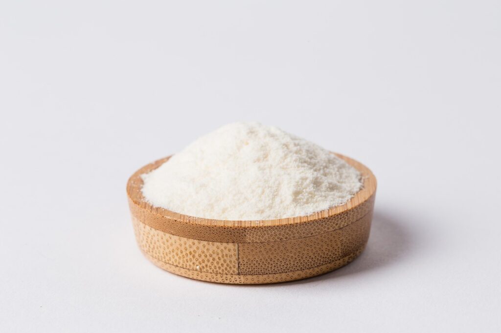 Small wooden bowl filled with a neat mound of milk powder against a plain light background.