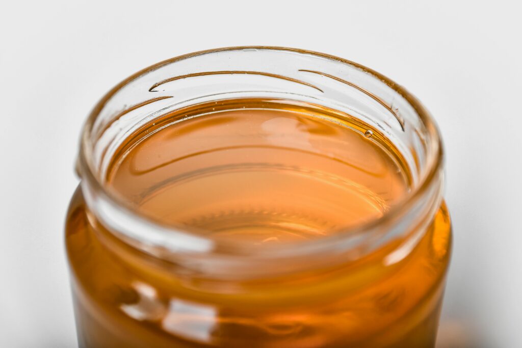 Open glass jar of golden honey photographed from above at an angle against a light gray background.