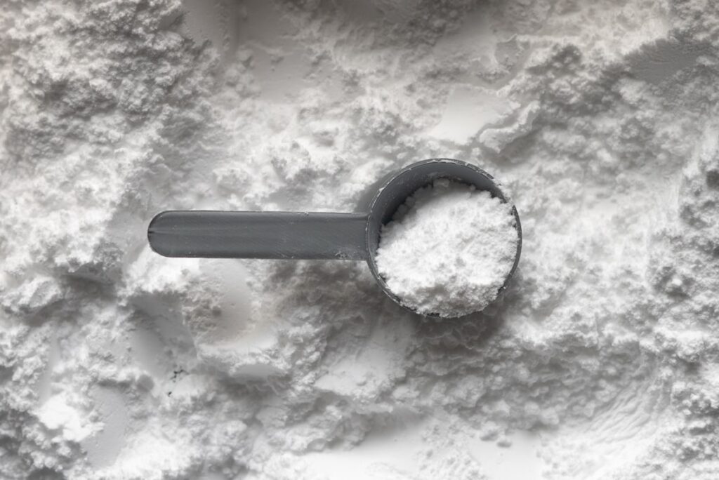Gray measuring scoop resting in a pile of fine cornstarch powder, photographed from above.