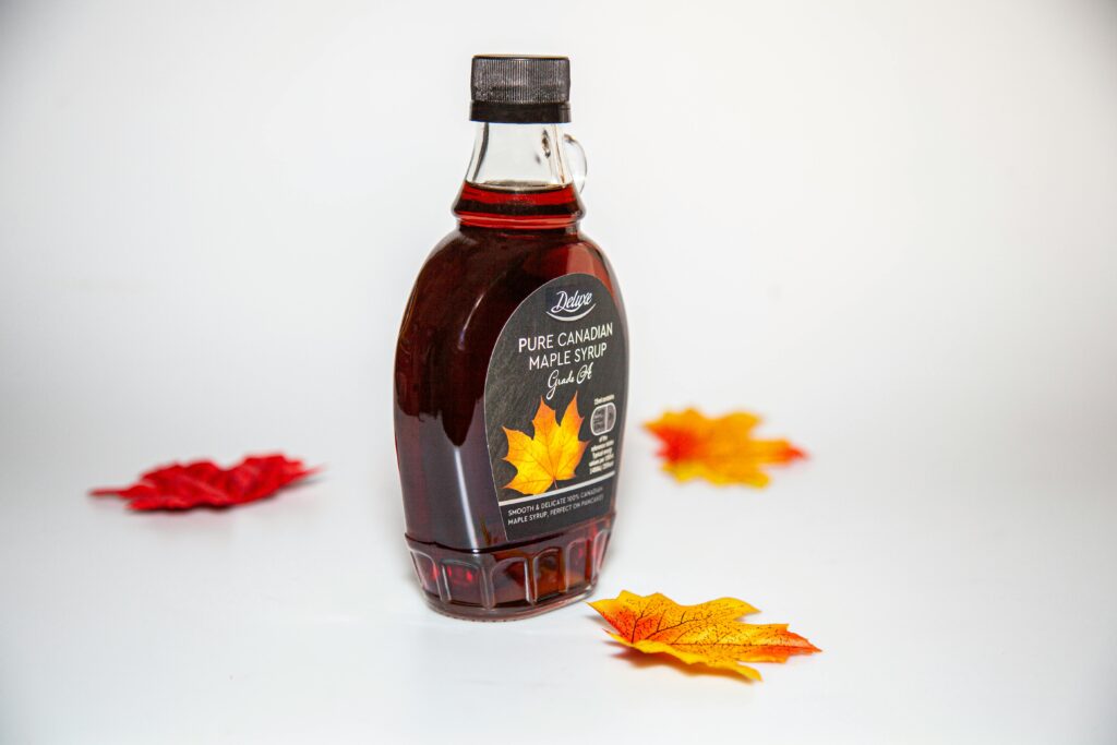 Plastic bottle of pure Canadian maple syrup on a white background, surrounded by scattered decorative red and orange maple leaves.
