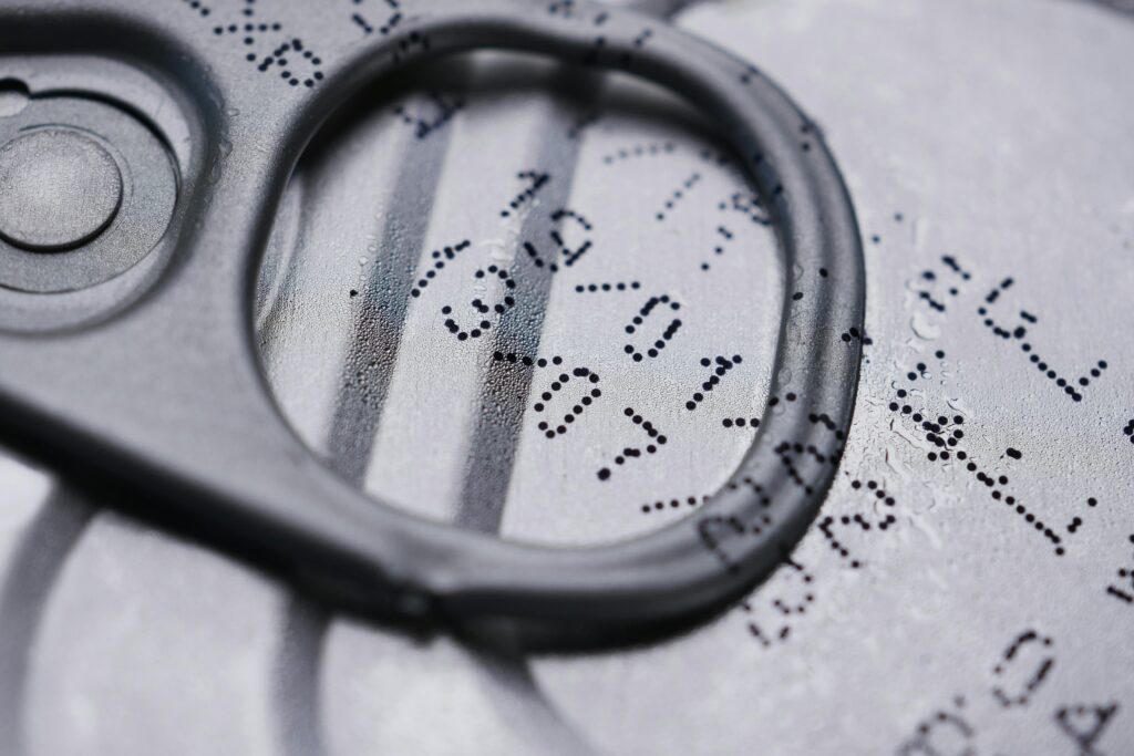 Extreme close-up of a metal can's pull-tab ring with stamped expiration date numbers visible on the aluminum surface.