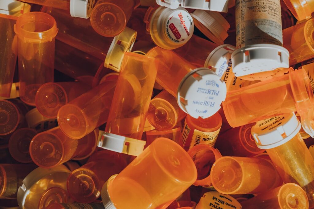 A large pile of empty amber prescription bottles with white childproof caps
