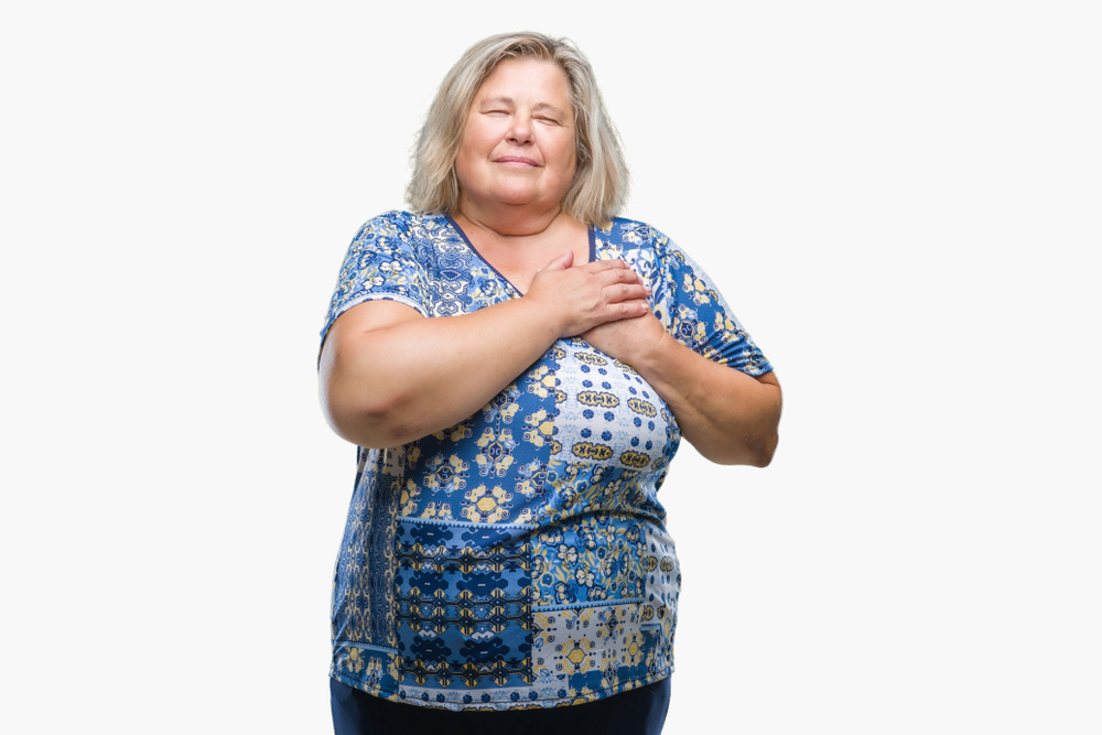 Senior plus size caucasian woman over isolated background smiling with hands on chest with closed eyes and grateful gesture on face. Health concept.