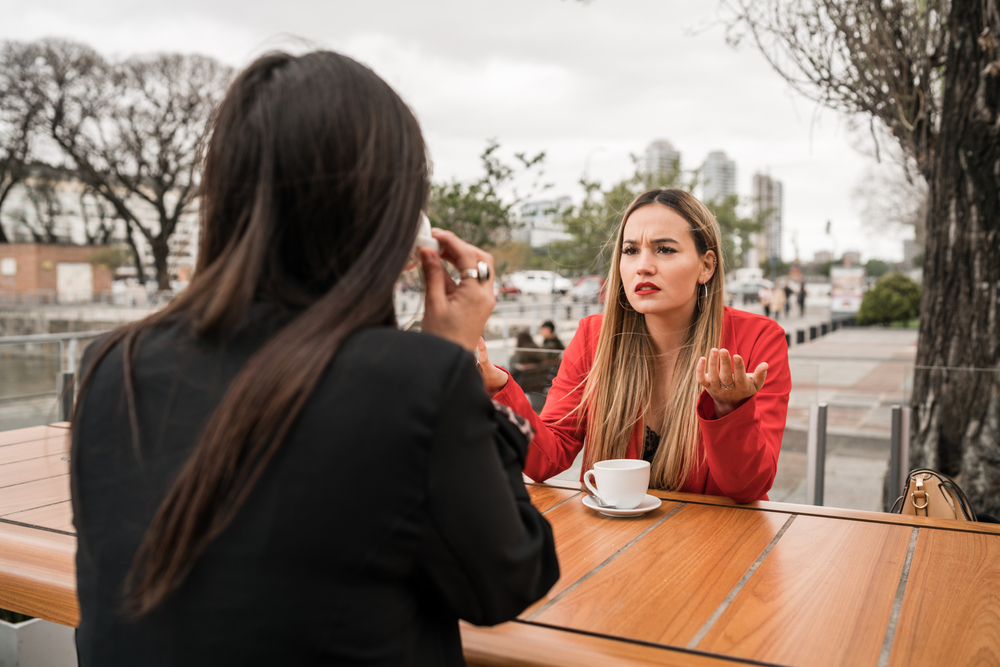 Portrait of two angry friends having a serious conversation and discussing while sitting at coffee shop. Friendship concept.
