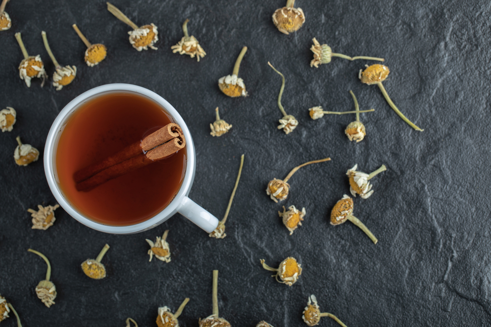 Cup of tea with cinnamon and pile of dried chamomiles