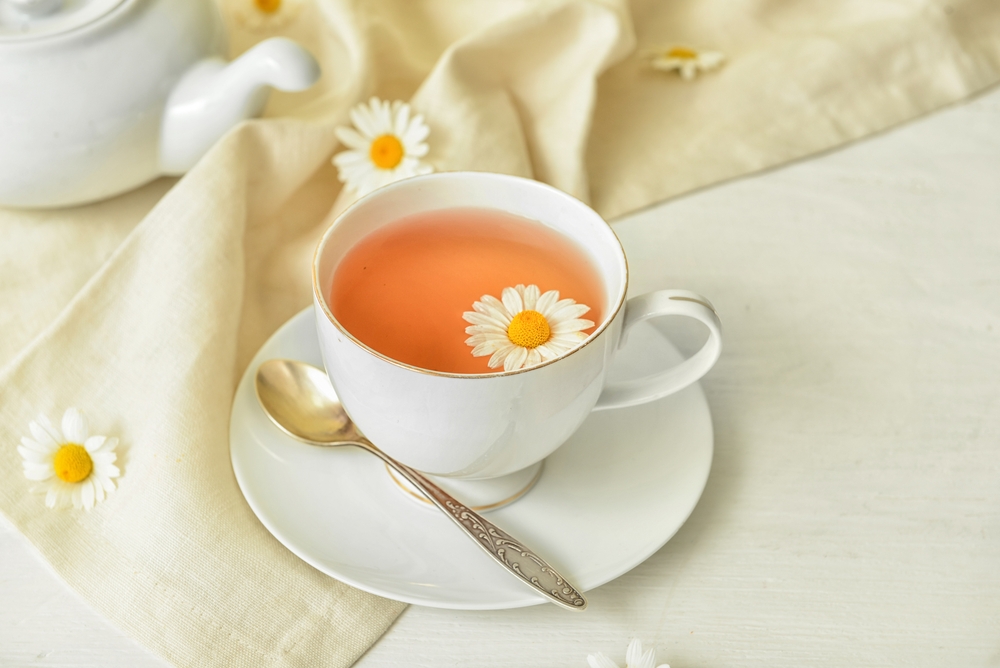 Cup of floral tea and flowers on light wooden background
