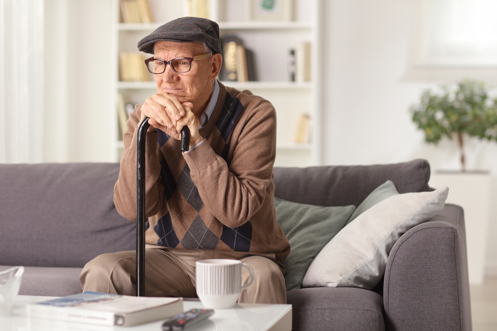 Grumpy elderly man sitting on a sofa with a walking cane at home