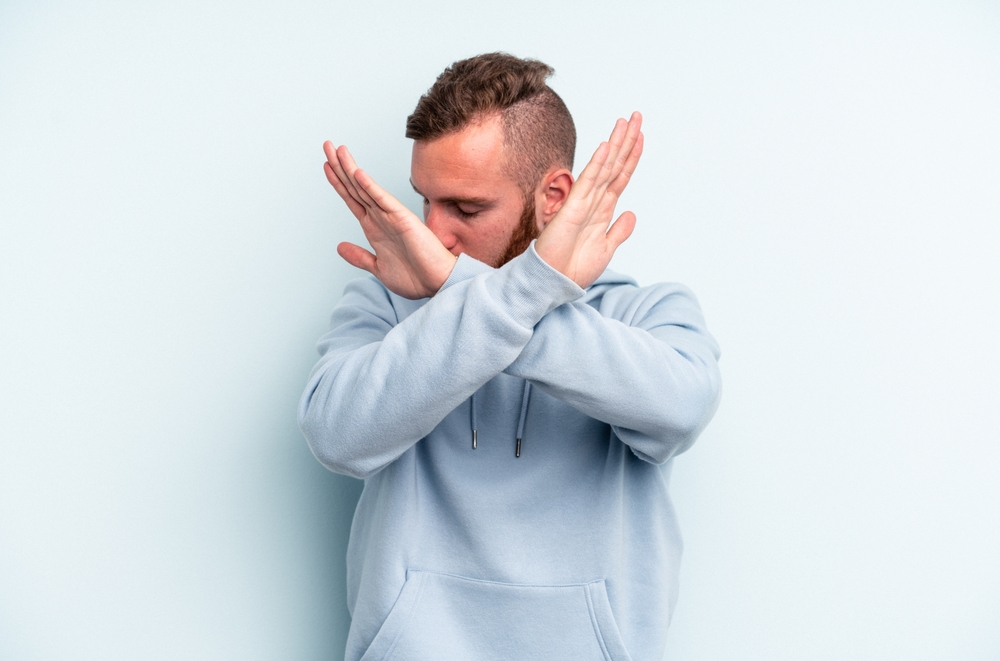 Young caucasian man isolated on blue background keeping two arms crossed, denial concept.