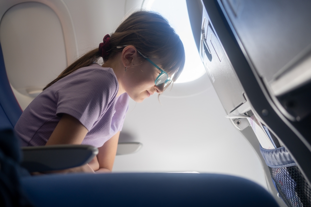 Young beautiful girl travels by plane with hand on stomach because nausea, painful disease feeling unwell. Ache concept. sick unhappy little child touching belly stomach with suffering from stomach