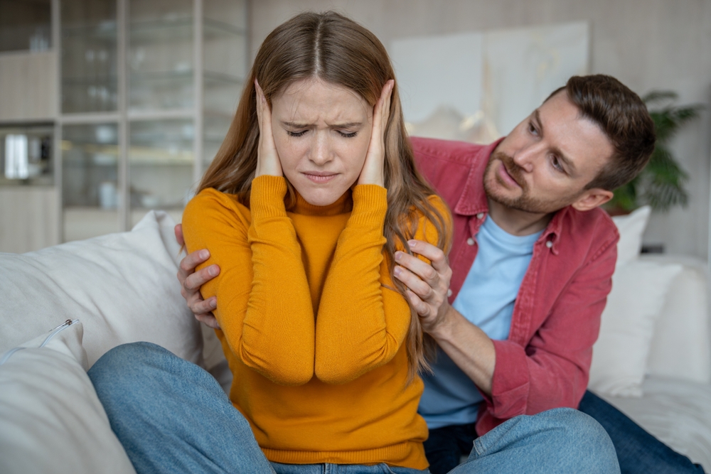 Disappointed woman sitting on sofa, closing ears with hands, doesnt want to hear man justifying, expaining disagreement in relations. Tension, emotional confrontation, misunderstanding in family life