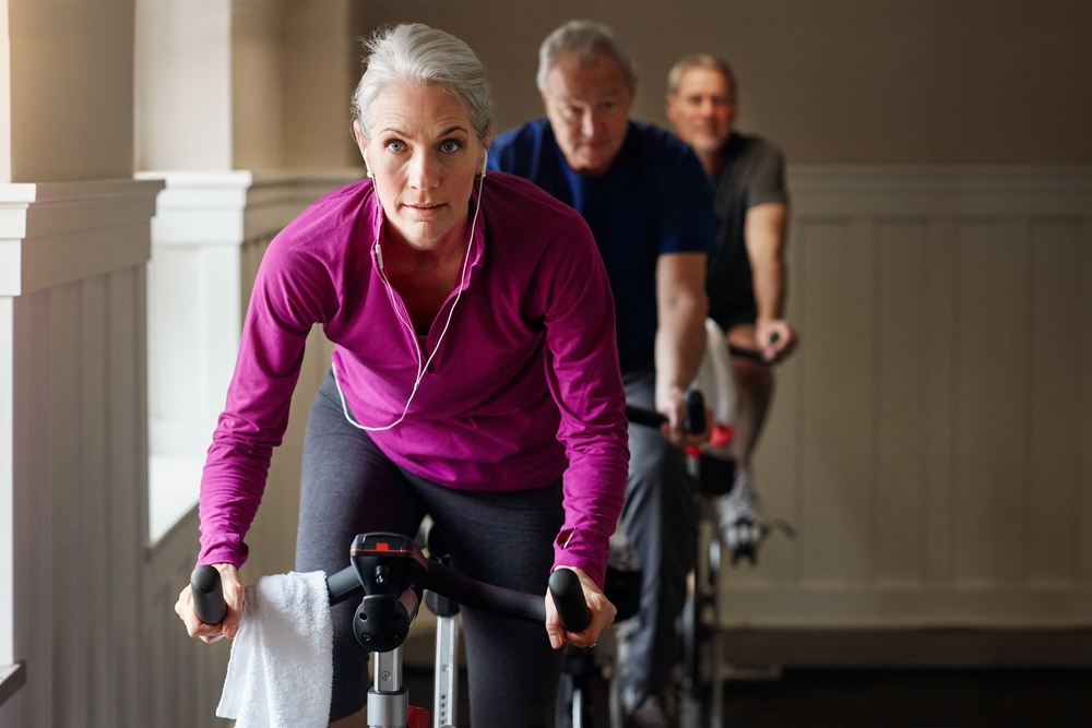 Spin class, fitness or senior woman on bike in workout or training for cycling progress, health or wellness. Group, challenge or confident elderly person on bicycle machine for gym or cardio exercise