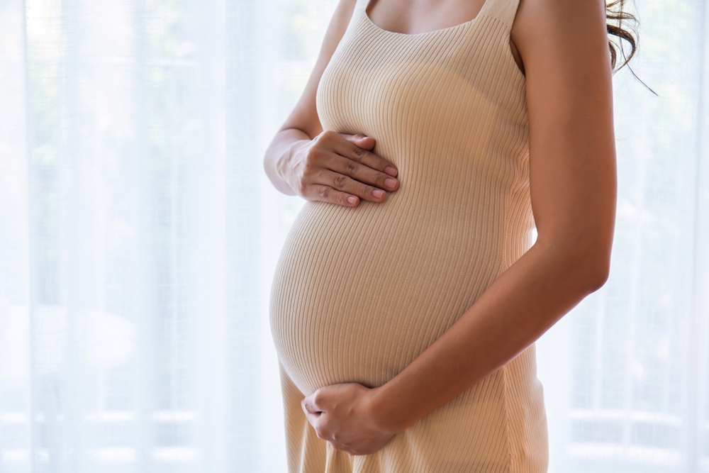 Pregnant woman standing with her hands gently rubbing her belly, showing love, warmth and concern for the baby