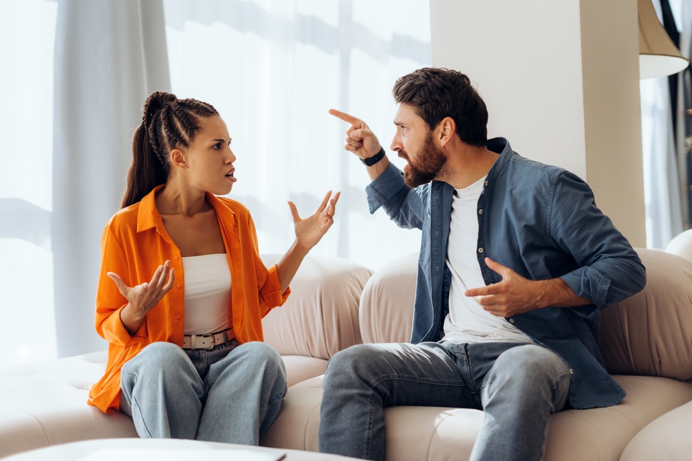 Portrait of angry, unhappy couple quarreling sitting on sofa at home, gesturing. Relationship concept, conflict