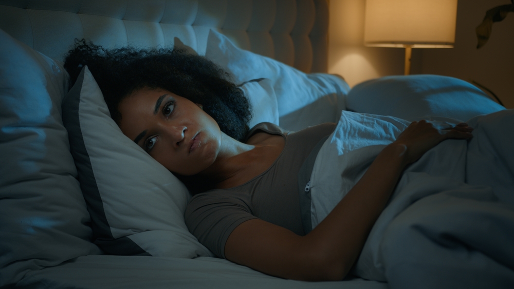 Noisy neighbours problem annoyed African American frustrated displeased woman lying in bed night dark bedroom suffer from sleeping disorder insomnia sleepless angry girl trying sleep awake from noise