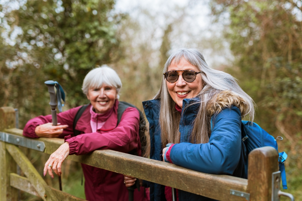 Two older women enjoying a hike in nature, smiling and wearing outdoor gear. They appear happy and relaxed, embracing the joy of hiking and nature. Happy senior women hiking in nature.