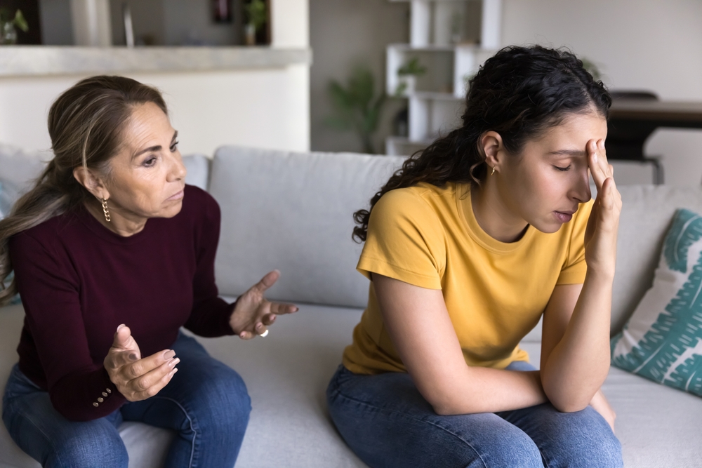 A tense moment between mother and daughter, family conflicts, misunderstandings, toxic relationships. 60 year old woman shouting, yelling at 20 year old daughter, fighting, quarreling at home sitting on sofa